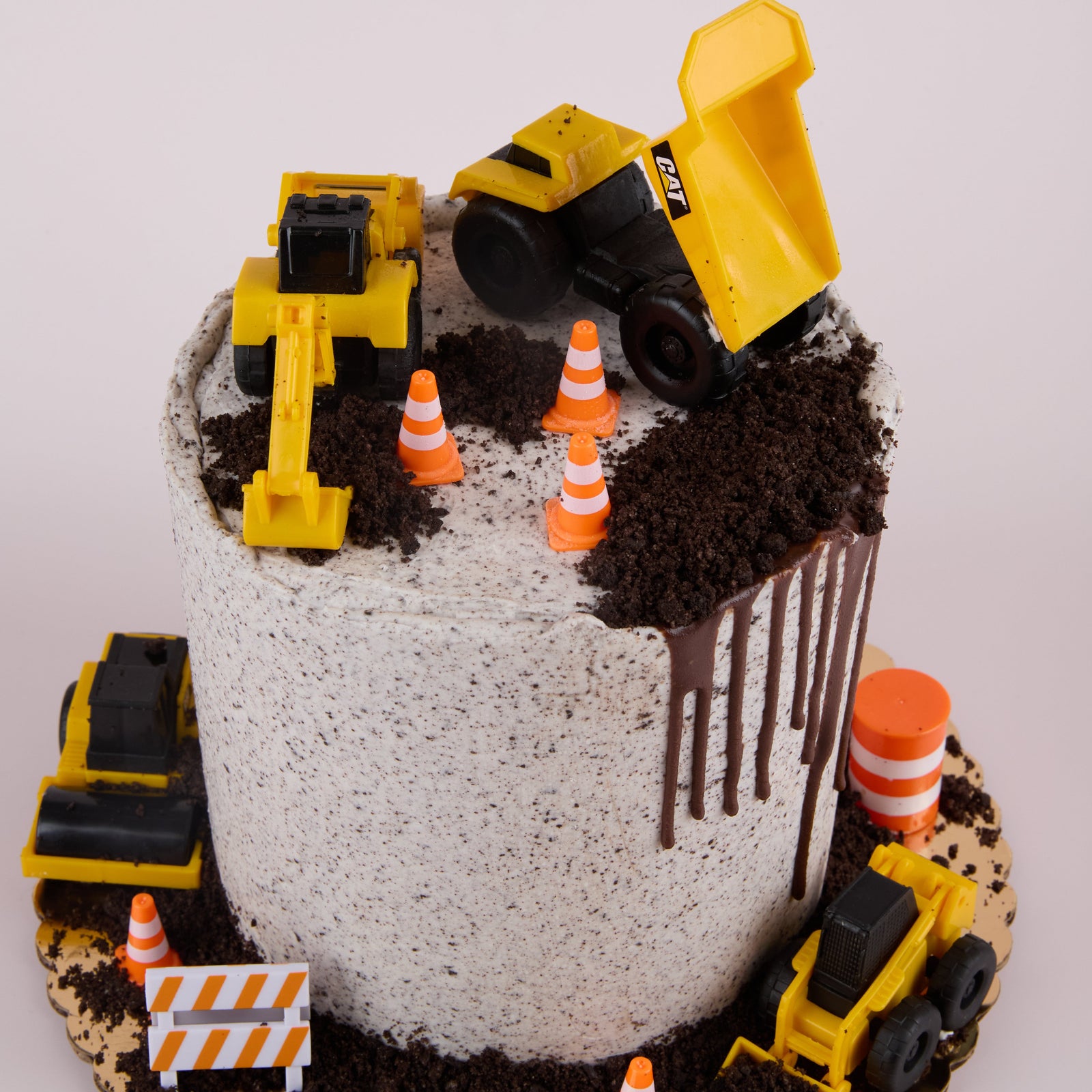Construction-themed birthday cake with toy dump trucks and traffic cones on a white background