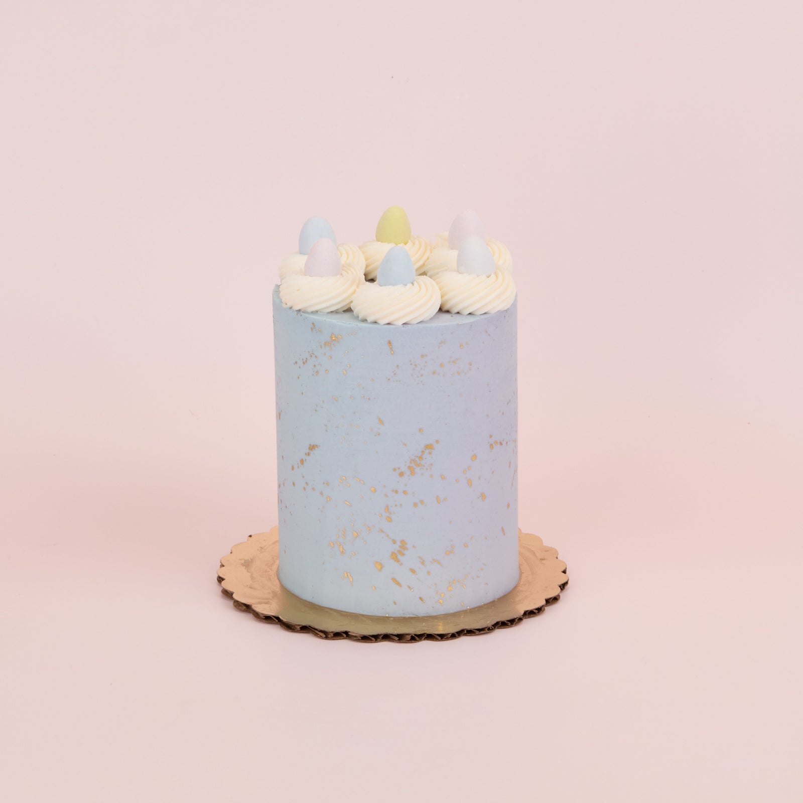 light blue cake with gold splatter, topped with vanilla rosette border and mini easter eggs 