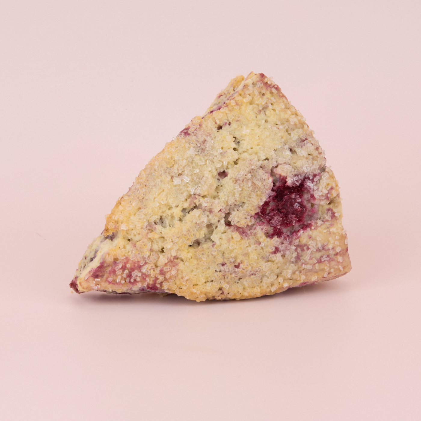 scone with a rapsberries and coarse sugar on a pink background