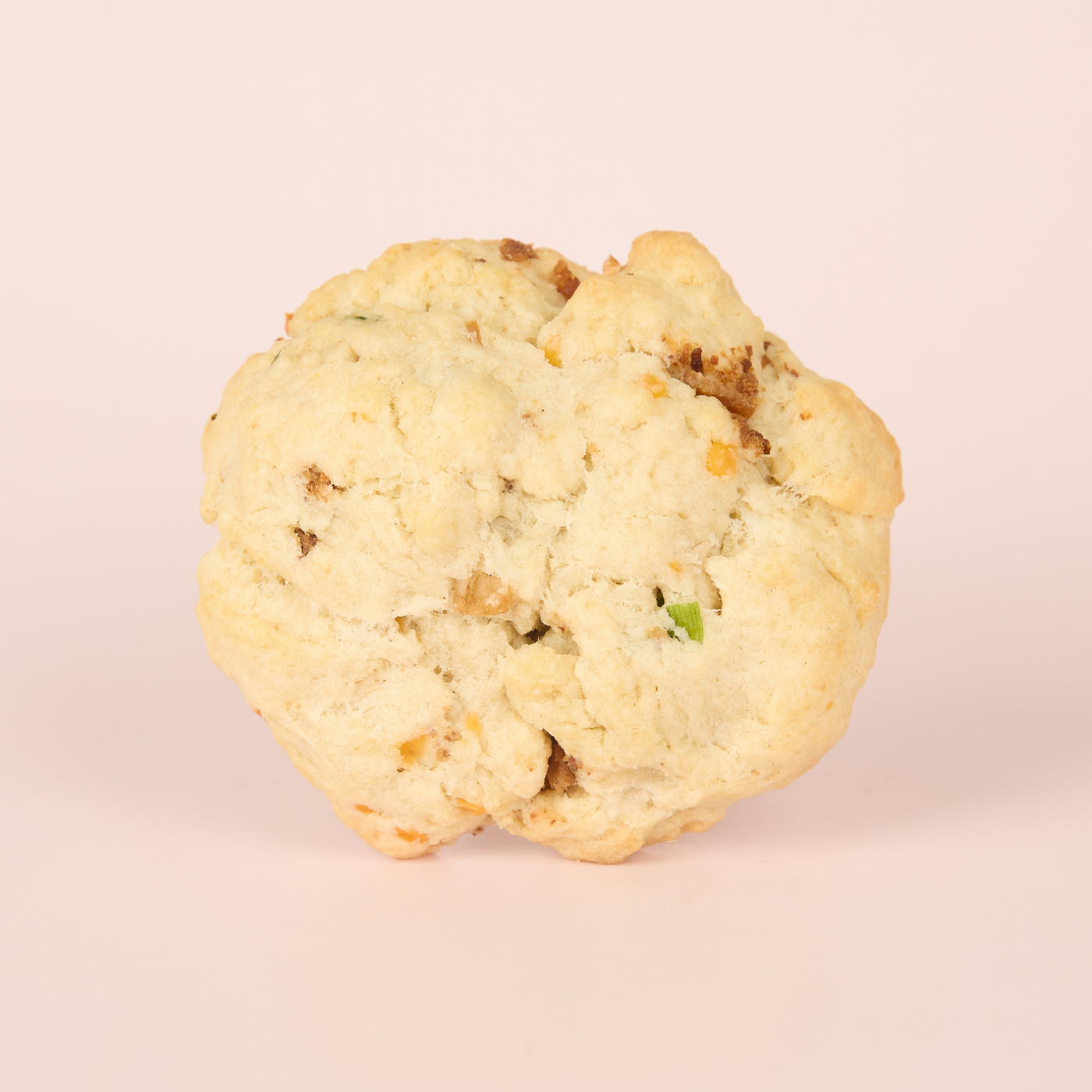 Single savory scone on a light pink background, bits of bacon and green onions throughout