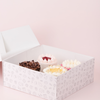 Open box containing three decorated mini cakes on a light pink background